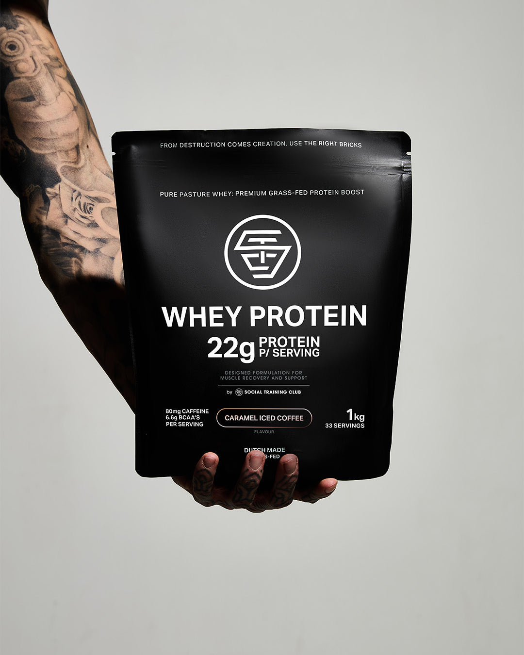 Hand holding a black whey protein package against a plain background.