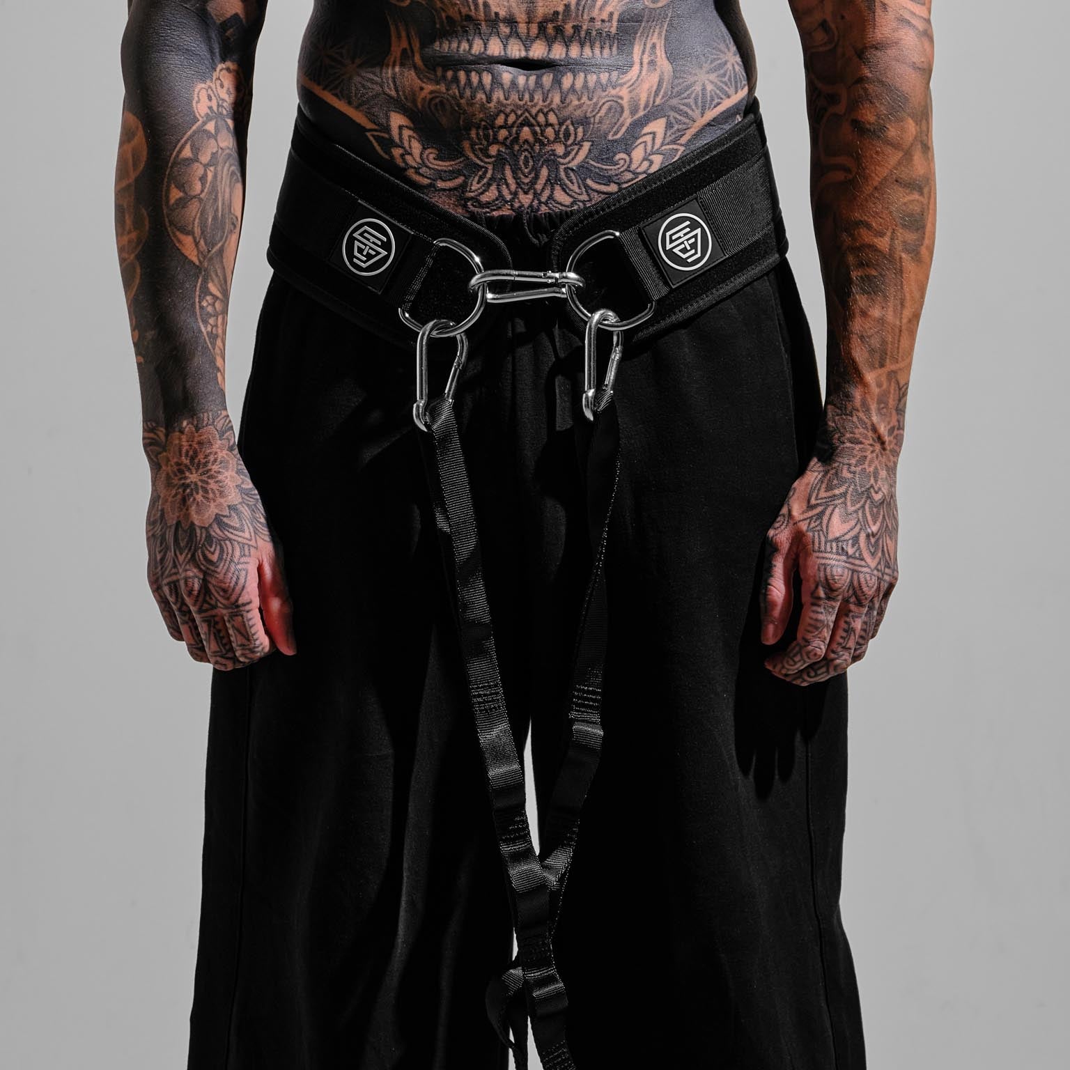 Person wearing black pants with a belt and carabiner on a gray background