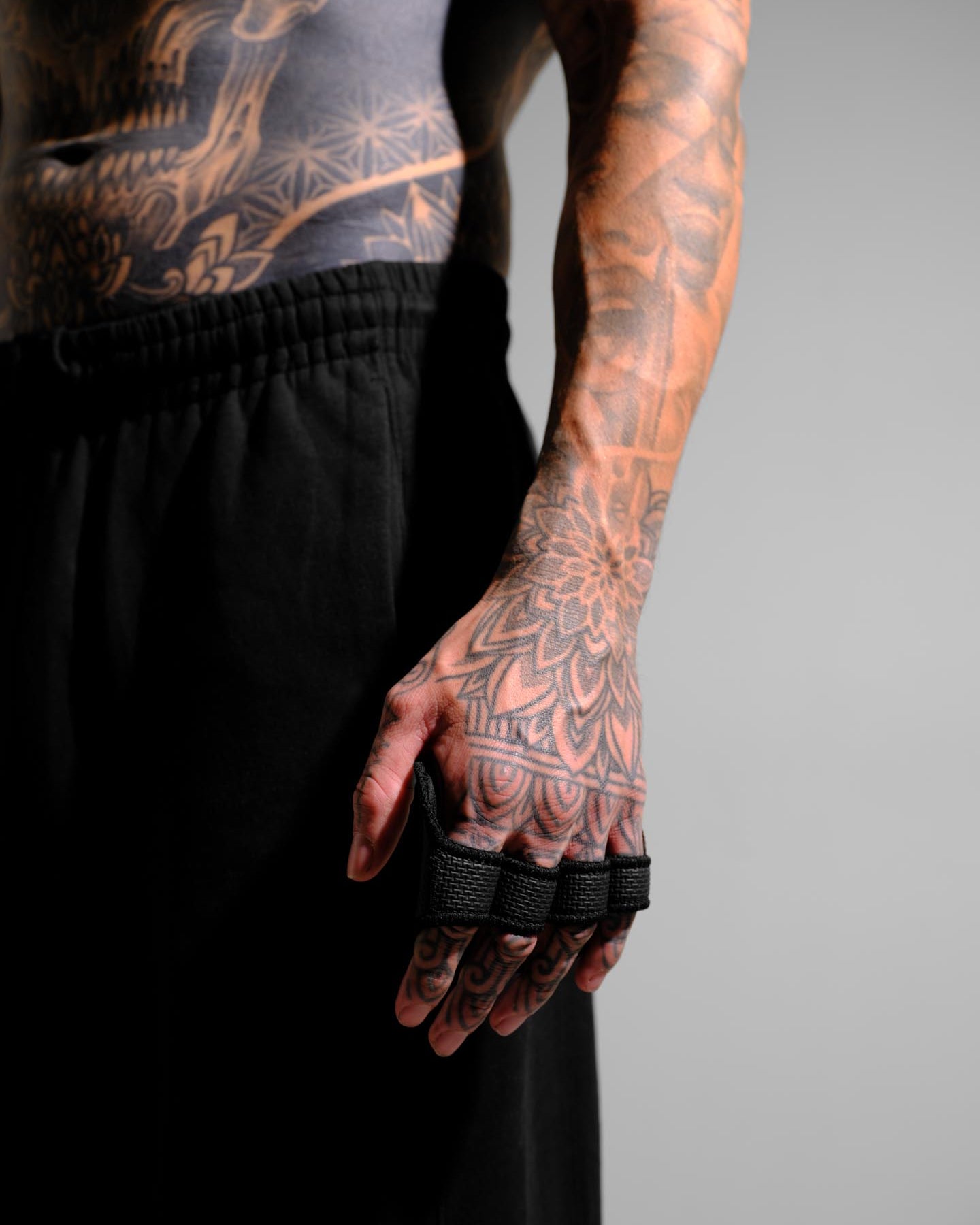 Person with tattoos wearing black grip pads on a gray background