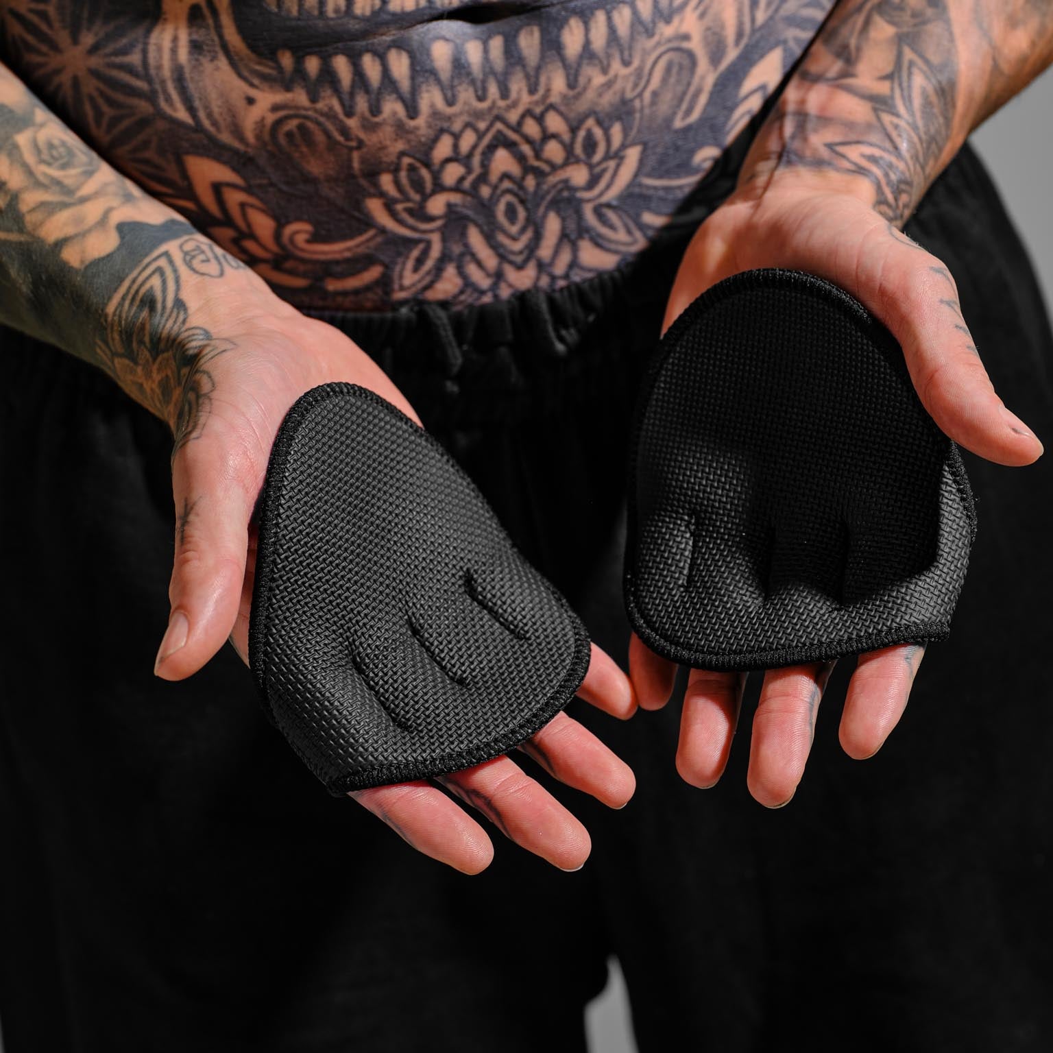 Person with tattoos wearing black grip pads on a gray background