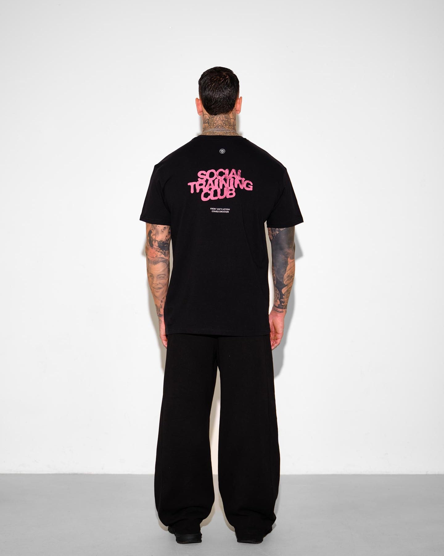 Person wearing a black t-shirt with 'Social Training Club' text on the back, standing against a white background.
