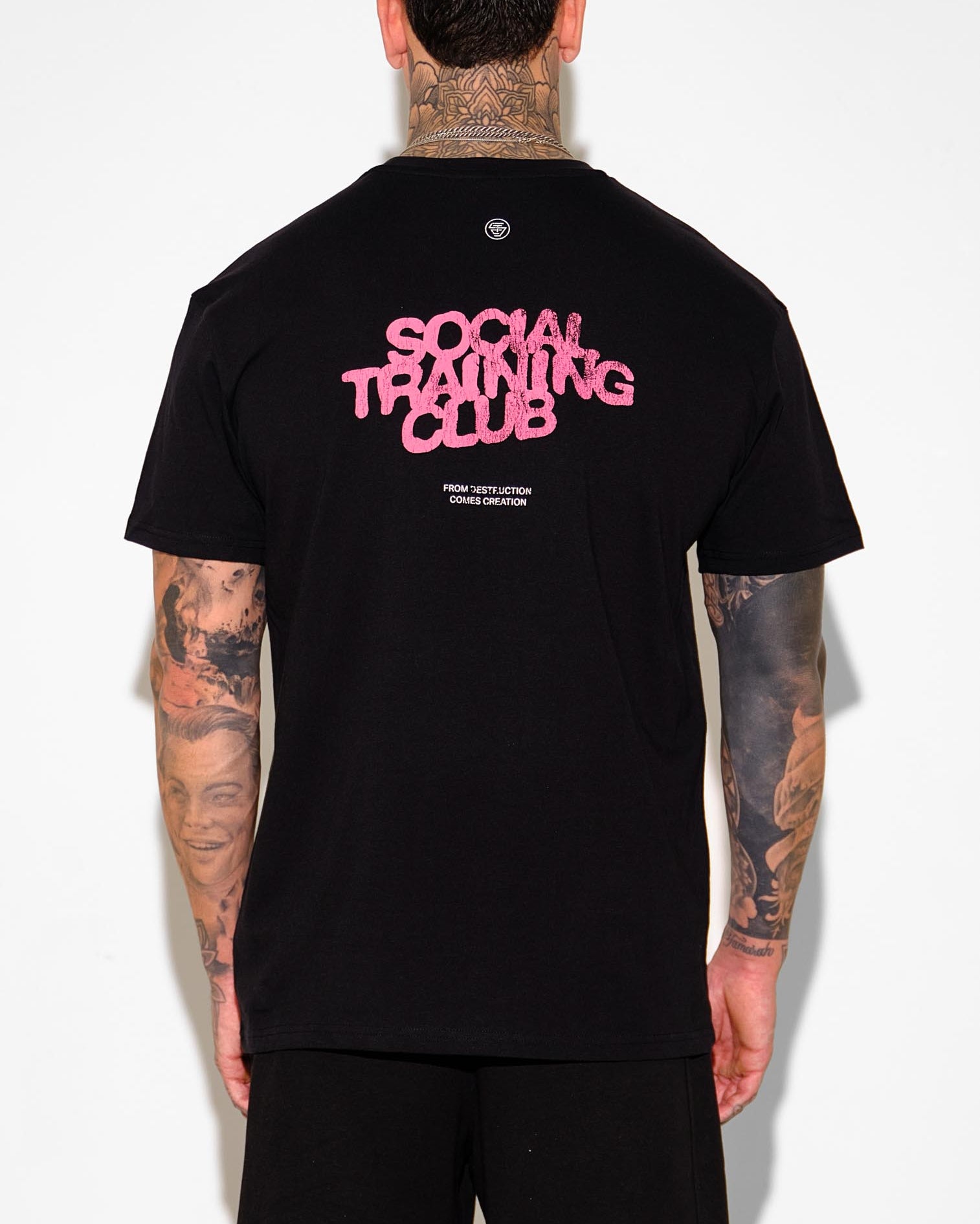 Person wearing a black t-shirt with 'Social Training Club' text on the back, standing against a white background.