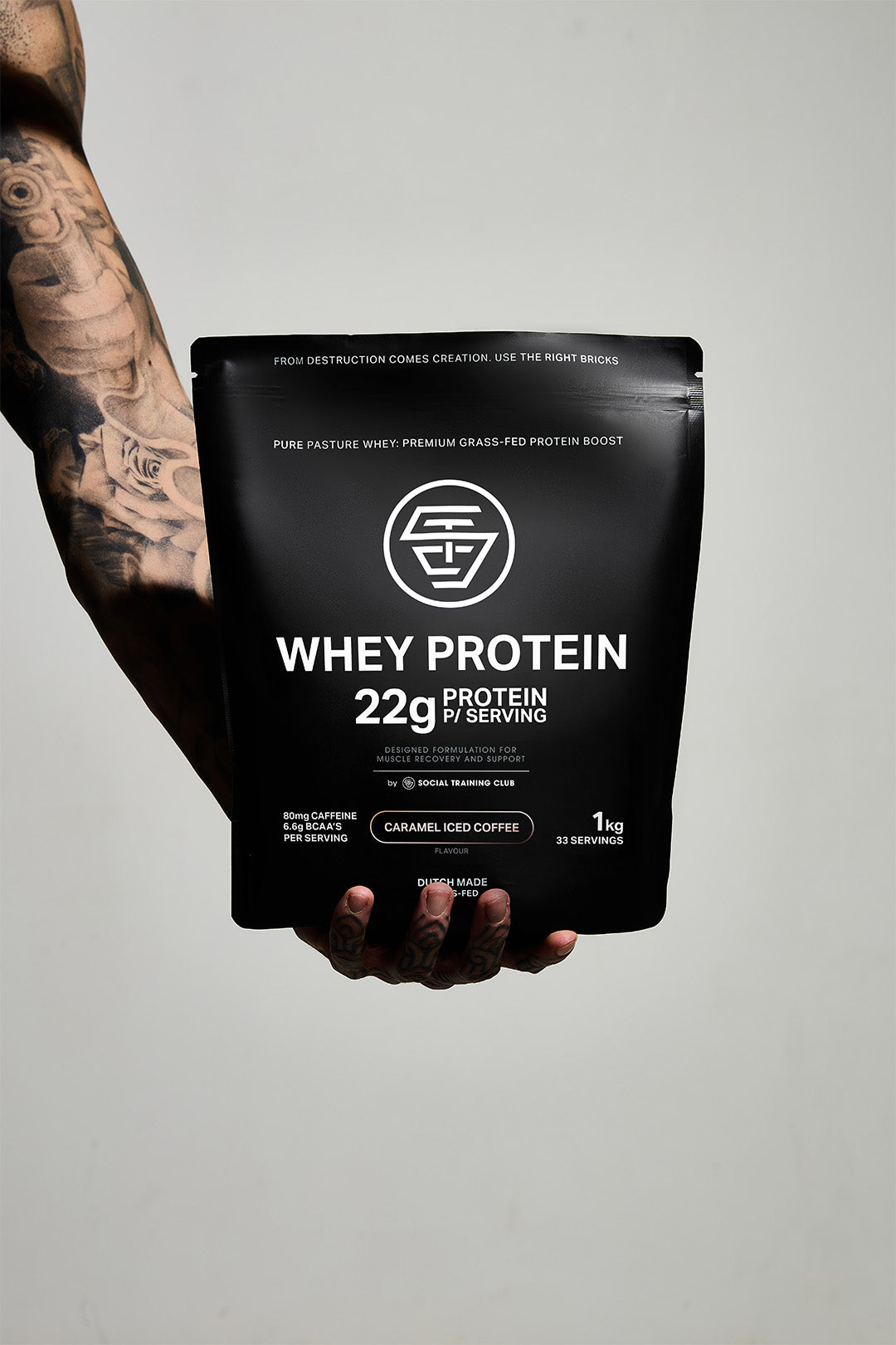 Hand holding a black whey protein package against a plain background.