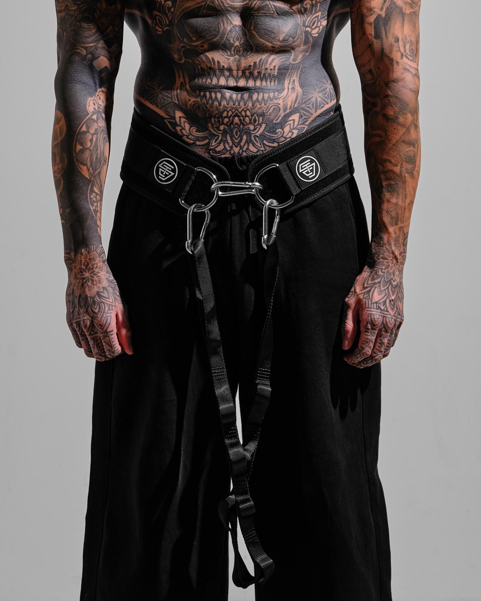 Person wearing black pants with a belt and carabiner on a gray background