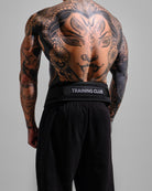 Person wearing a black 'Training Club' belt with tattoos on a gray background