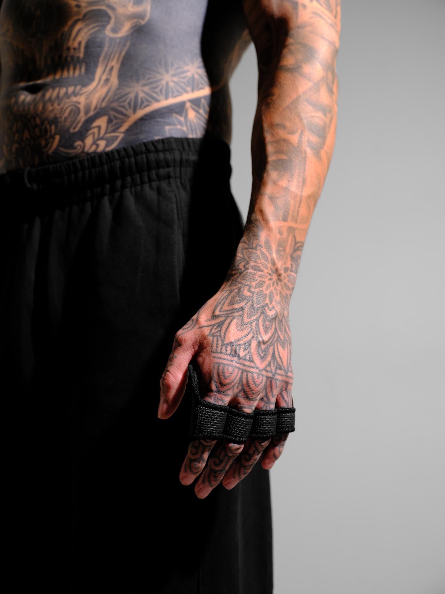 Person with tattoos wearing black grip pads on a gray background