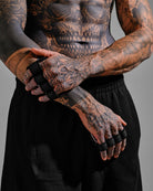 Person with tattoos wearing black grip pads on a gray background