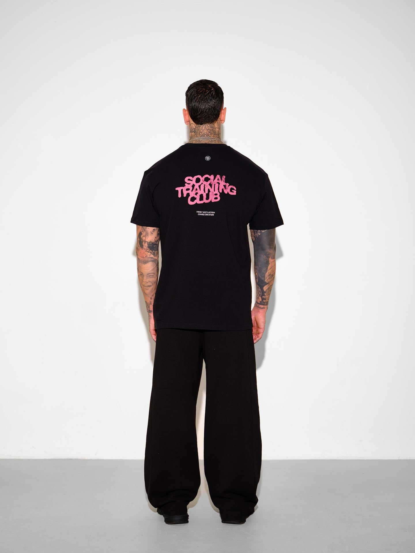 Person wearing a black t-shirt with 'Social Training Club' text on the back, standing against a white background.